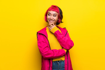 Young woman with pink hair over yellow wall looking to the side