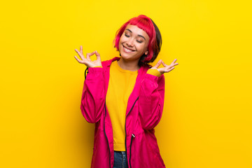 Young woman with pink hair over yellow wall in zen pose