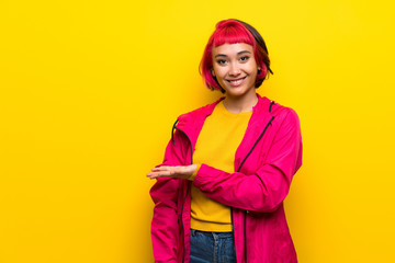 Young woman with pink hair over yellow wall presenting an idea while looking smiling towards