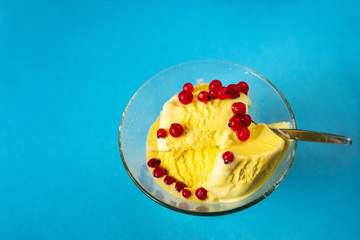 Vanilla ice cream with red currant berry in dewy glass cup on blue.