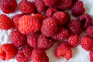 Big ripe raspberries are laying on the  table covered with white tablecloth