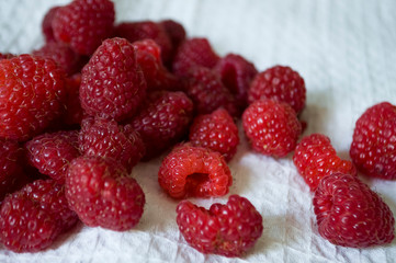 Big ripe raspberries are laying on the  table covered with white tablecloth