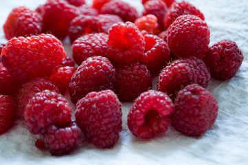Big ripe raspberries are laying on the  table covered with white tablecloth