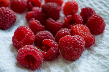 Big ripe raspberries are laying on the  table covered with white tablecloth