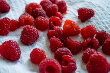 Big ripe raspberries are laying on the  table covered with white tablecloth