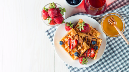 Fototapeta na wymiar Photo of fresh homemade food made of berry Belgian waffles with honey, chocolate, strawberry, blueberry, maple syrup and cream. Healthy dessert breakfast concept with juice. 