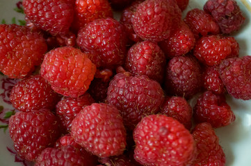 Big ripe raspberries are laying on the  table covered with white tablecloth