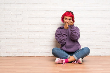 Young woman with pink hair sitting on the floor making money gesture