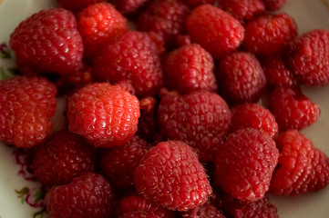 Big ripe raspberries are laying on the  table covered with white tablecloth