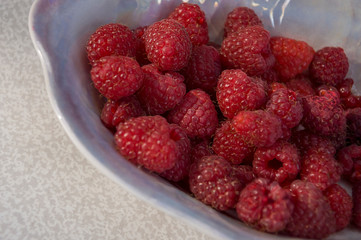 Big ripe raspberries are laying on the  table covered with white tablecloth