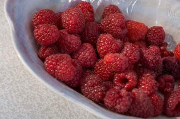 Big ripe raspberries are laying on the  table covered with white tablecloth