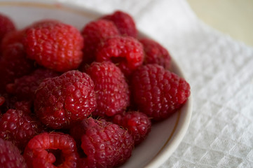 Big ripe raspberries are laying on the  table covered with white tablecloth