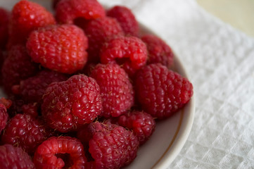 Big ripe raspberries are laying on the  table covered with white tablecloth