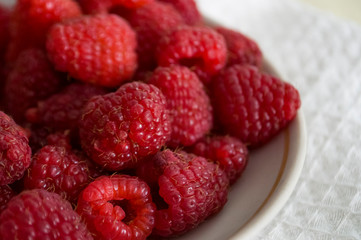 Big ripe raspberries are laying on the  table covered with white tablecloth