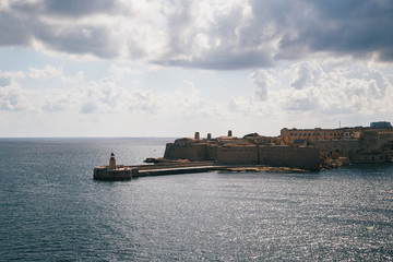 Fototapeta premium View of the Grand Harbour entrance and old medieval Ricasoli East Breakwater with red lighthouse and Fort Ricasoli seen from Valletta, Malta