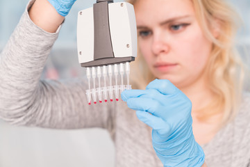 Close up of Young female scientist working in genetics laboratory with pipette in white biological...