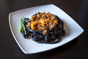 black pasta with cuttlefish ink. Pasta of durum wheat semolina with squid ink with beef and sweet pepper sauce on a square plate