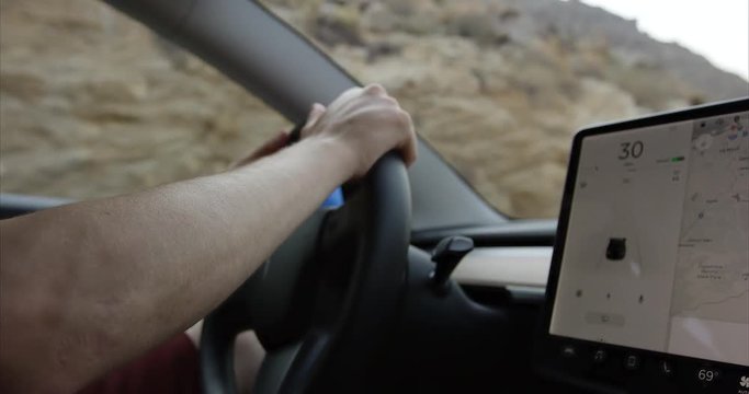 Young man driving modern car in desert- close up on hands and console
