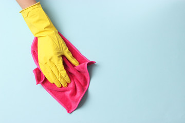 female hand in cleaning glove and rag on colored background