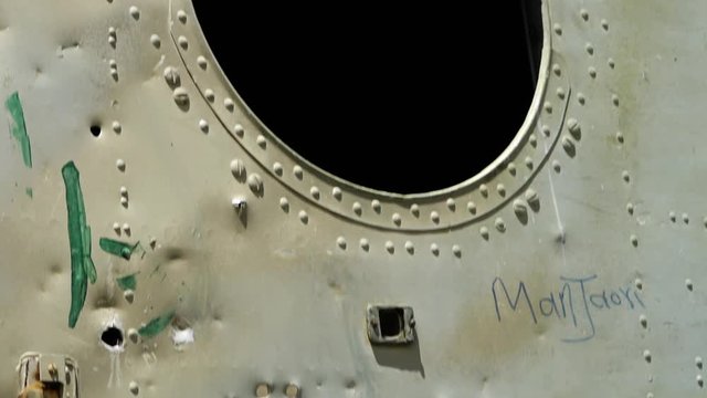 A hand held, tilting, extreme close up shot of a metal scrap which has gunshot holes in it.