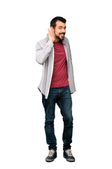 Fototapeta premium Full-length shot of Handsome man with beard listening to something by putting hand on the ear over isolated white background