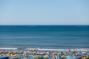 Beach with bathers and sailboats in the sea