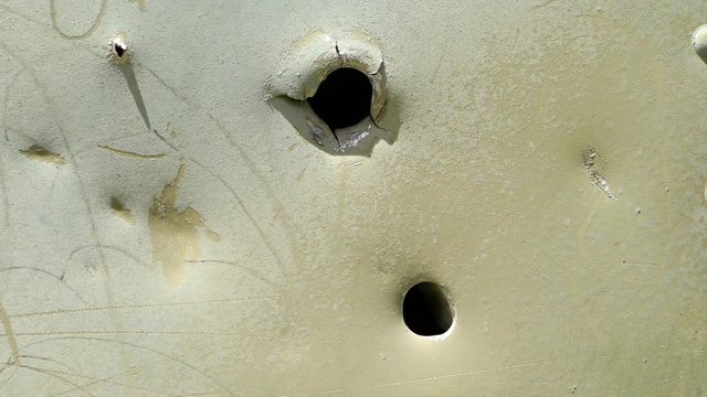 A steady, extreme close up shot of some holes torn in a white metal piece.
