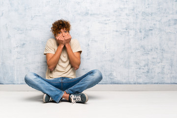 Young african american man sitting on the floor nervous and scared putting hands to mouth