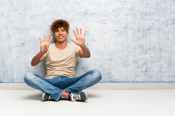 Young african american man sitting on the floor counting nine with fingers