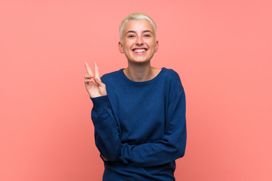 Teenager girl with white short hair over pink wall smiling and showing victory sign