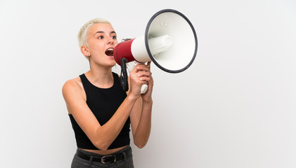 Teenager girl with short hair over white wall shouting through a megaphone