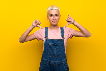Fototapeta na wymiar Teenager girl with overalls on yellow background showing thumb down