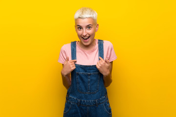 Teenager girl with overalls on yellow background with surprise facial expression