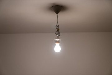 naked lit light bulb hanging from the ceiling of a dimly lit room
