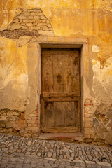Close-up of an old wooden door of an abandoned building with a scraped orange wall damaged by time, Piedmont, Italy