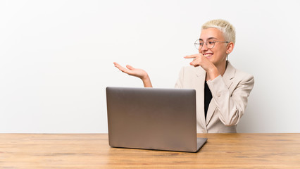 Teenager girl with short hair with a laptop holding copyspace imaginary on the palm to insert an ad