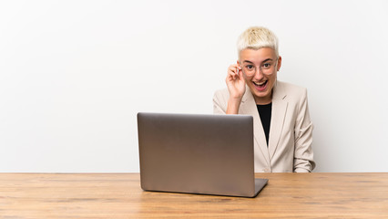 Teenager girl with short hair with a laptop with glasses and surprised