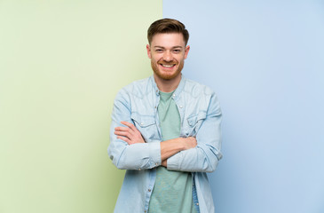 Redhead man over colorful background keeping the arms crossed in frontal position