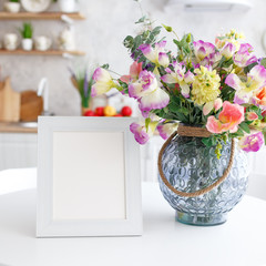 Wooden decorative frame on a white table with a bouquet of flowers.