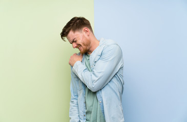 Redhead man over colorful background suffering from pain in shoulder for having made an effort