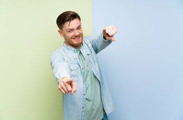 Redhead man over colorful background points finger at you while smiling