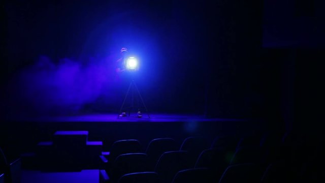 A man illuminator directs a beam of light from a profile spotlight from the stage to a gymnasium in clouds of smoke. Overall plan