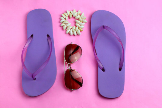 Beach purple beach flip flops, aviator sunglasses, seashell bracelet on a pink background. Summer colorful  travel beach flat lay