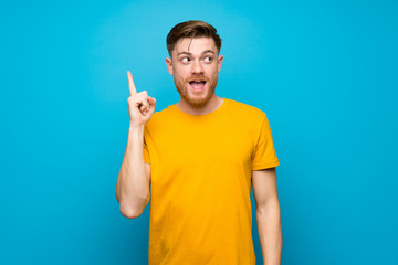Redhead man over blue wall intending to realizes the solution while lifting a finger up - obrazy, fototapety, plakaty