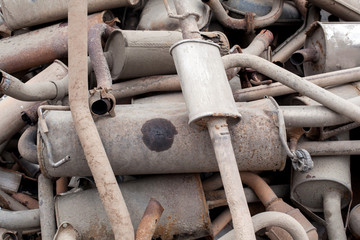 Close view pile of used mufflers at car workshop. Lot of exhaust pipes stacked in absolutely no order