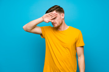 Redhead man over blue wall with tired and sick expression