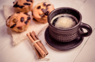 Hot morning coffee, cinnamon sticks and three muffins on wooden background