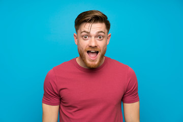 Redhead man on isolated blue wall with surprise facial expression