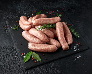Freshly made raw butchers sausages in skins with herbs on stone board