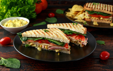 Sandwich with ham, cheese, tomatoes, spinach, corn, mayonnaise, mustard, gherkins, toasted bread and potato chips.